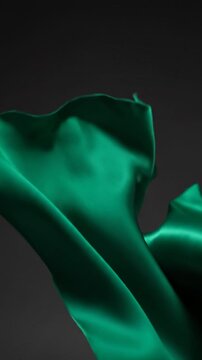 Elegant emerald silk satin fabric background, flowing wavy textile drape, smooth glossy soft material texture, luxury abstract motion design