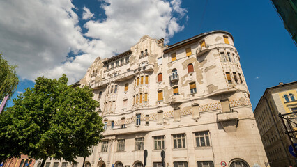 Naklejka premium Historic Eclectic Revival apartment building in Budapest with cream-colored facade, ornate architectural details, and distinctive rounded tower corner. Classic early 1900s European urban architecture.