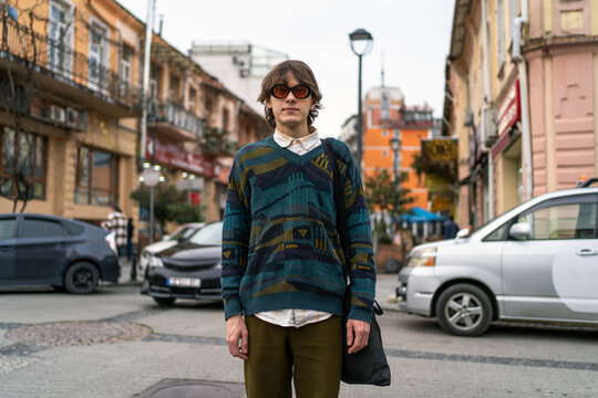 Gen Z retro fashion young man standing on city street, hipster sunglasses, street style, urban youth lifestyle, travel mood.