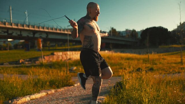Man jumps rope in a park near a bridge during the evening with sunlight shining down on the grass and pathways