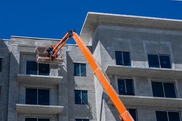 Construction Worker on Orange Boom Lift Elevating to Apartment building under construction © Francisco