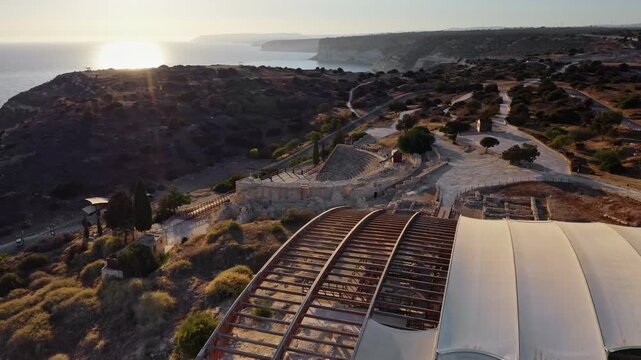 Kourion archaeological site on Cyprus coast with ancient ruins and modern canopy at sunset, aerial view showcasing historic theater, stadium and coastal landscape preservation. Drone flight