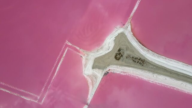 High angle drone shot of a stunning pink mineral lake with clouds reflecting perfectly on the water surface. Scenic aerial landscape of natural salt evaporation ponds.
