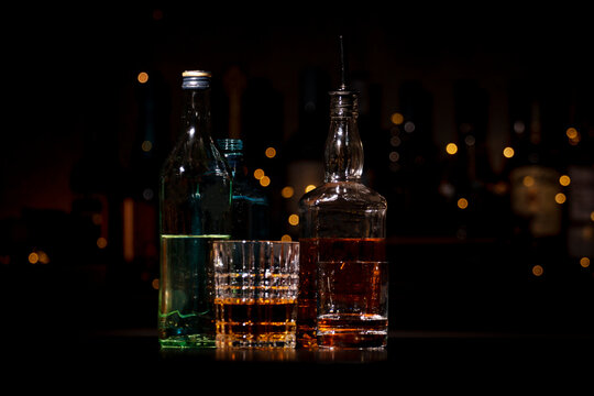 Bottles of gin and bourbon near glasses with strong alcohol on bar counter. Nightlife atmosphere and high quality spirits selection.