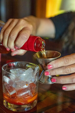 Hands pour liquid into a jigger over a glass with ice