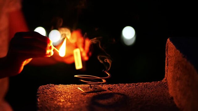 Person lighting mosquito repellent coil with match at night