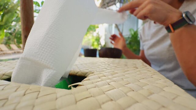 Woman Pulling a Tissue From a Woven Tissue Box at an Outdoor Tropical Cafe During a Relaxed Morning Breakfast