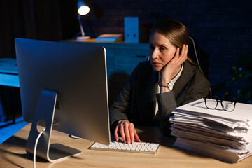 Workaholic. Overwhelmed woman in suit working with computer near stack of documents at wooden desk...