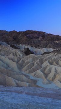 Vertical Screen: Death Valley National Park Zabriskie Point California showcases dramatic eroded mudstone badlands during blue hour twilight with layered sedimentary ridges and deep shadows.