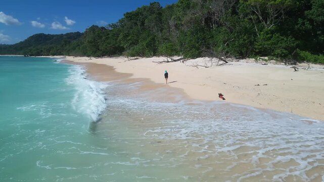 Woman jogging by ocean shore. Vibrant seaside scene with woman running along foamy waves. Bright sky over turquoise waters as woman jogs along sandy coastal edge