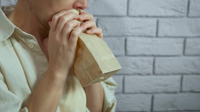 Woman breathing into paper bag during panic attack. Anxious woman hyperventilating and breathing into a paper bag to regulate her breathing during a panic attack or anxiety episode
