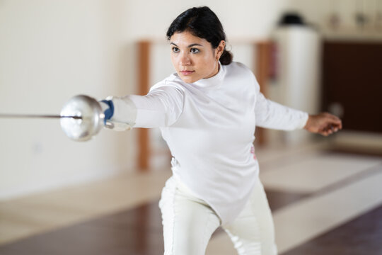 Female athlete training attack movements with rapier at fencing workout