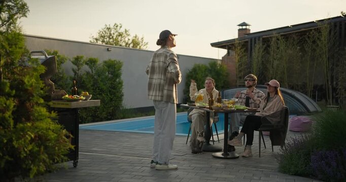 Backyard poolside gathering with people talking at an outdoor table in warm evening light