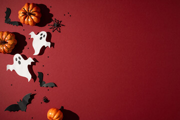 Naklejka premium Happy Halloween scene with paper ghost cutouts, mini pumpkins and black bat decorations on red background