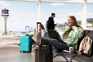 Obraz premium Digital nomad girl working remotely on laptop in the airport waiting area, Gen Z location independent with virtual office and global mobility, Modern online job and freedom of travel lifestyle.