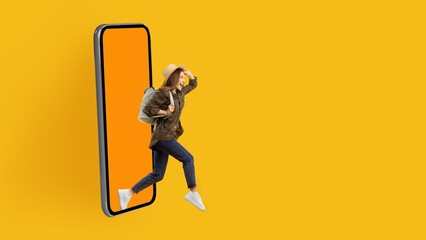 Joyful Young Asian Woman Stepping Out Of Smartphone With Bright Yellow Background, Embarking On A New Adventure Full Of Possibilities. Embracing Technology And Connection In Modern Lifestyle. © Prostock-studio