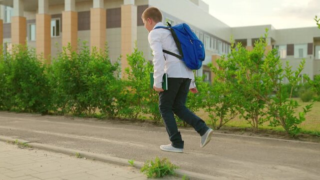 Boy student runs to school for lesson along sidewalk on city street. Child with book, backpack hurries to school. Child boy Running with textbook in his hand. Concept of children's education, learning