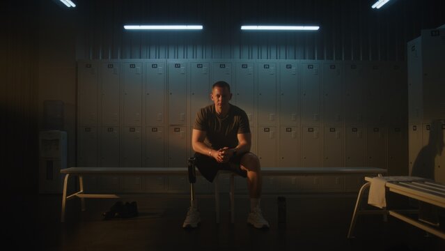 Young Adaptive Athlete in Sports Facility, Sitting With Clasped Hands and Bowed Head. Reality of Recovery and Resilience of People With Physical Disabilities. Strength and Vulnerability. Portrait.