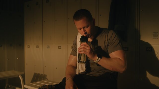 Athlete with Prosthetic Leg Resting in Sunlit Locker Room After Workout. Young Man Drinking Water, Wiping Sweat with Towel, and Breathing Heavily. Rehabilitation, Inclusion, Adaptive Sports Lifestyle.