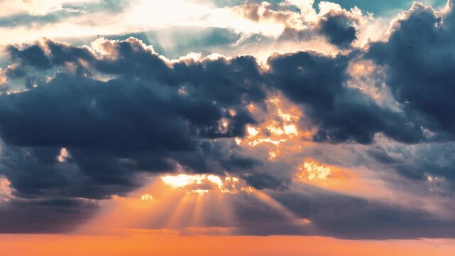 Bright sunbeams breaking through dark dramatic storm clouds during golden hour sunset sky with crepuscular rays.