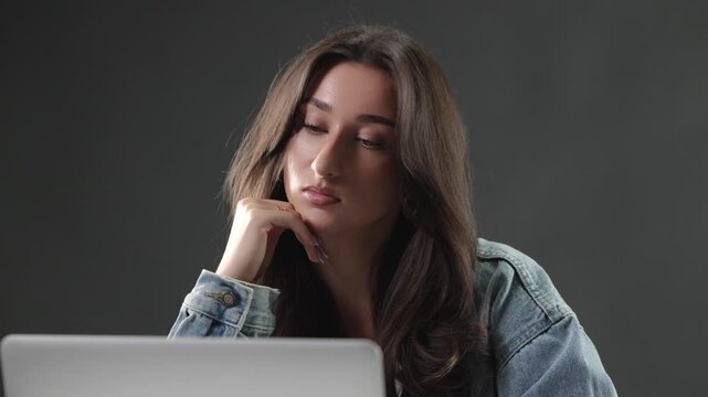 Remote work burnout and digital fatigue are evident as a young woman works on her laptop with a tired and stressed expression. This studio shot captures the challenges of modern work life balance, onl