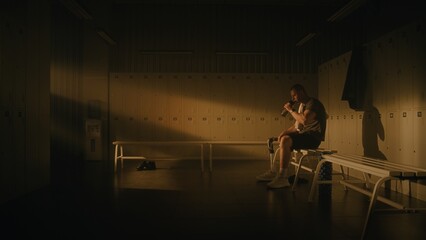 Fototapeta premium Reality of Hard Work. Tired Young Man With Prosthetic Leg Sits on Locker Room Bench After Intense Workout. Male Takes Sip of Water and Wipes Face With Towel, Resting in Warm Glow of Gym Setting Sun.