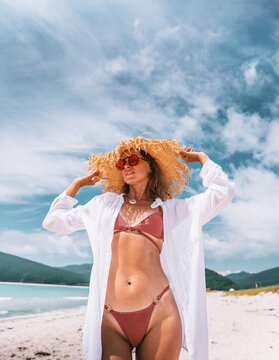 Modern female traveler showcases chic beach outfit against scenic shoreline and blue sky. Fashion, leisure and premium vacation experiences blend into aspirational summer lifestyle imagery.