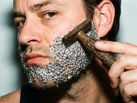 Man shaving beard with metallic mercury droplets on face using razor.