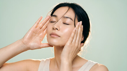 Naklejka premium Woman with wet hand gently touching face on mint green background in studio