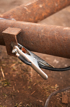 Detailed view of welding clamp fixed to rusty metal beam in outdoor workspace. Image represents hands-on craftsmanship, equipment preparation and successful DIY fabrication projects.