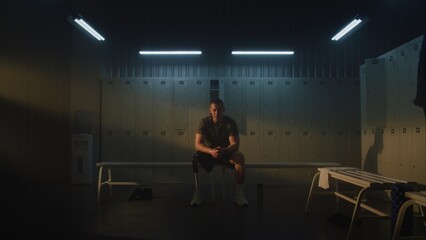Fototapeta premium Young Man with Prosthetic Leg Sits on Bench in Dimly Lit Locker Room, Focusing Mind and Building Motivation Before Standing Up to Start Workout Session. Mental Grit and Determination. Portrait.