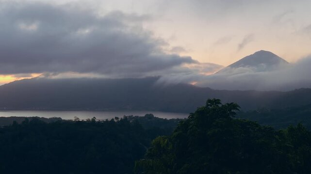 Mount Abang And Lake Batur Beneath Flowing Clouds at Early Sunrise, Soft Morning Light Illuminates Volcanic Highlands And Lush Forested Terrain