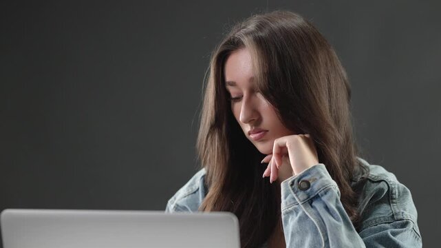 Burnout and mental fatigue concept, a young woman works on her laptop with an exhausted and stressed expression. Challenges of remote work, overwork, and the importance of work life balance for studen