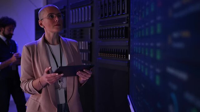 Female it specialist working on a server rack in a modern data center using a tablet for network administration