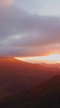 Vertical video. Spectacular Sunrise Above Mount Abang And Gunung Batur, Golden Light Breaks Through Dramatic Clouds Over Lake Batur And Dense Tropical Forested Highlands