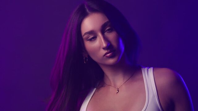 Confident young woman with dark hair and bold makeup in studio lighting, fashion and beauty portrait. The woman looks directly at the viewer with a serious expression. Her long dark hair frames her fa