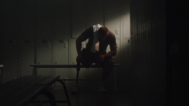 Following Intense Session, Athlete With Limb Loss Retreats to Dressing Room to Restore Energy. Man Sits Down Wearily, Leaning Against Lockers as Beam of Natural Light Fills Space. Inclusive Wellness.