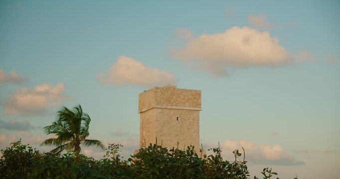 Stone watchtower Faro de Tulum rises above palms near Caribbean coast at sunset in Mexico