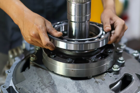 Close-up of mechanic hands carefully installing a large metal ball bearing onto a steel transmission shaft during mechanical repair.