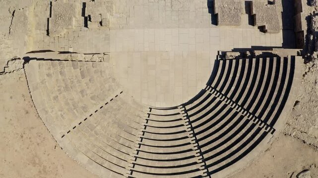 Ancient Kourion theater curved stone seating and orchestra floor, with strong sunlight casting dramatic shadows on the steps of the historical Roman amphitheater in Limassol. Aerial view drone shot