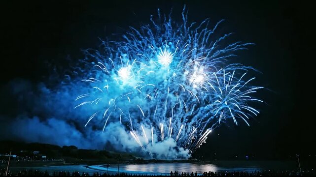 Spectacular blue fireworks explode in the night sky over a calm lake, celebrating a festive event