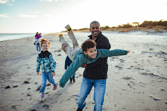 Father playing airplane with son on beach at sunset