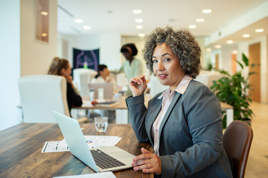 Confident senior businesswoman working on laptop in modern open office