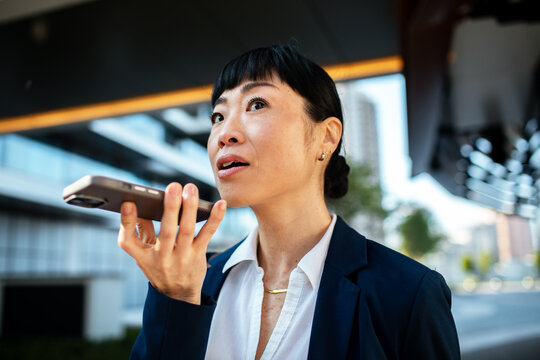 Businesswoman using smartphone voice assistant outdoors downtown
