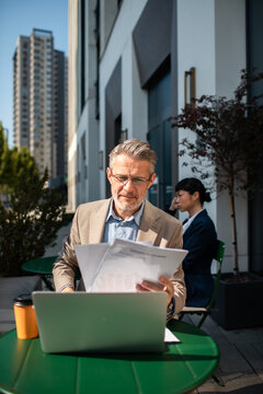 Senior executive reviewing reports on laptop at outdoor city cafe
