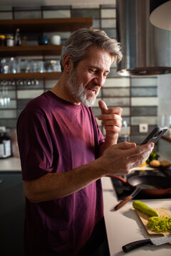 Middle-aged man using smartphone for recipe while cooking in home kitchen