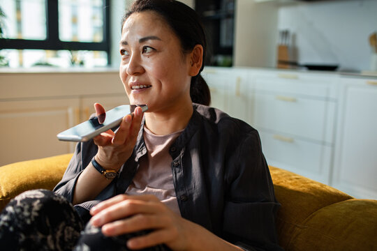 Smiling woman using voice command on smartphone at home