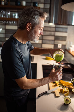 Middle-aged man pouring green smoothie in home kitchen