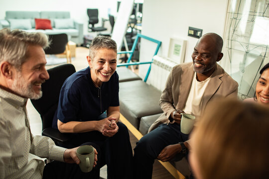 Diverse coworkers chatting over coffee in modern office lounge