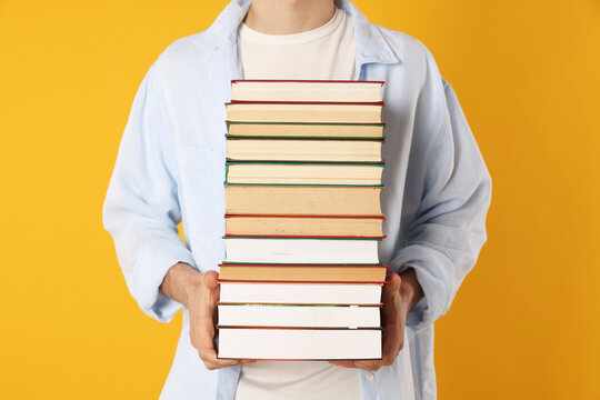 Teenage boy with stack of books on orange background, closeup